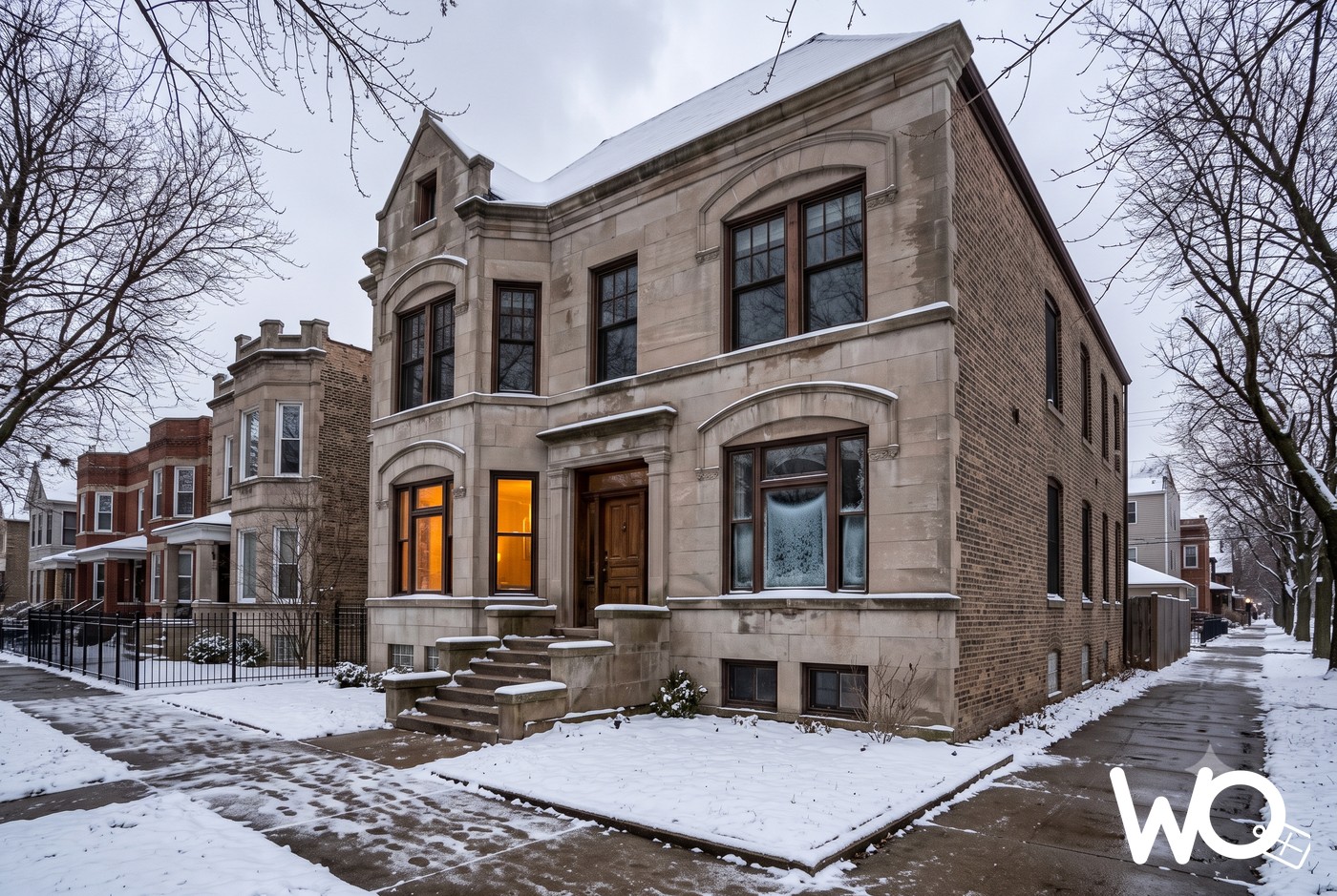 A classic Chicago greystone home in winter with light snow, older wood windows, and one window glowing warm against the gray sky