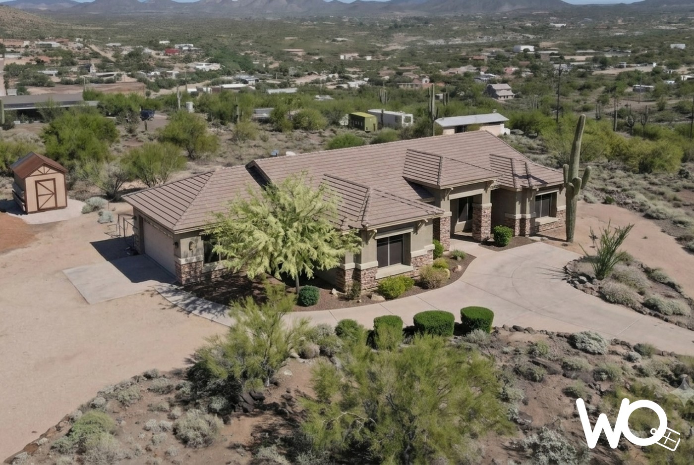 A southwestern adobe home in Phoenix under bright desert sun, with saguaro cacti and the Superstition Mountains behind it